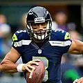 Headshot of Russell Wilson in uniform and helmet running with the football