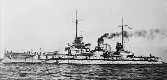 A large warship steams at low speed; gray smoke drifts from the two smoke stacks