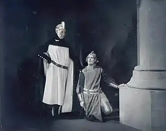 man standing and woman kneeling in prayer in stage setting depicting a huge cathedral