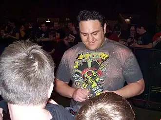 A dark-skinned adult male wearing a multi-colored T-shirt signing an autograph