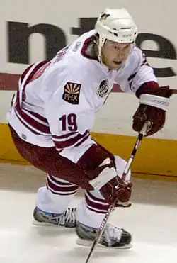 Doan skating, wearing hockey gear and holding a stick