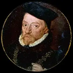 On a square black frame is a golden circle with a photo of a man with a brown beard and black garments with a white ruff on a starry background.