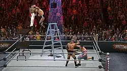 A shirtless masked wrestler attempts to slam a wrestler wearing blue and white striped shorts through two stacked tables, another wrestler waring jean shorts and sneakers punches a fourth wrestler who is holding his head. All four are in a wrestling ring with a ladder at the center and a briefcase hanging above the ladder, in front of a crowd.