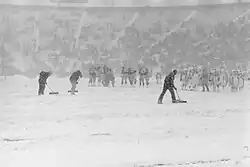 Black and white photo of snow on Lambeau Field during the game, getting cleared by a worker