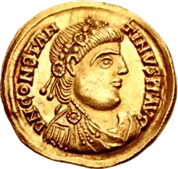 A gold coin showing the profile of a man with two strings of beads in his hair.