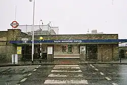 A brown-bricked building with a rectangular, dark blue sign reading "SOUTH WOODFORD STATION" in white letters all surrounded by snowflakes