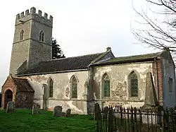 A church in stone, partly rendered, seen from the southeast, showing the battlemented tower, the south porch, and the nave and chancel, both with lancet windows