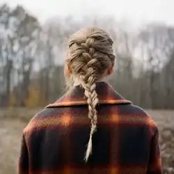 Cover artwork of evermore, a photo of Swift's back showing her braided hair and flannel shirt. She is seen standing in front of a barren field