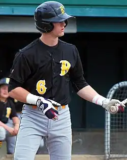 Ward standing at home plate and holding his bat in his left hand before a pitch is thrown. He is wearing an Anchorage Bucs uniform, a black jersey with a gold "B" logo and the number 6.