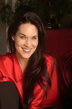 Teal Swan wearing a bright red top, grinning directly at camera