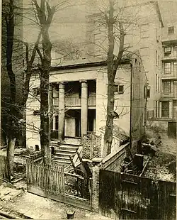 Black and white photograph of a small Greek revival house in an alleyway