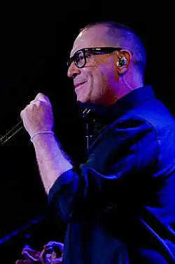 profile of Torquil Campbell standing on a dark stage, wearing a dark shirt, appearing to sing or speak into a microphone