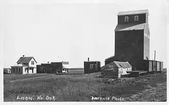 A black and white photo of a farmhouse with a grain elevator in the background. The text "Lithia, No. Dak. Bjorngas Photo" is written on the bottom of the photo.