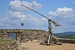 Photo of a reconstructed medieval trebuchet on a stone platform against a cloudy sky in the background