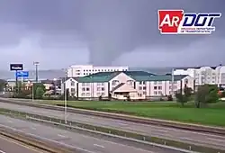 The large tornado passing behind a building in daylight.