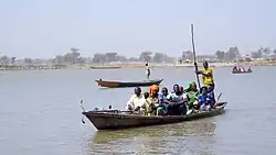 A large stream of black water rippled with a few ripples passes under a blue sky and white clouds.