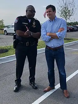Two men look toward the camera and gesture as if talking
