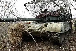 PT-91 tank with anti-drone metal mesh in the Ukrainian 117th Heavy Mechanized Brigade, surrounded by trees in daytime