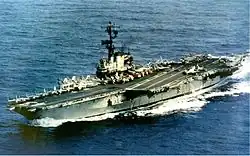 Medium-size aircraft carrier with numerous aircraft on its flight deck.