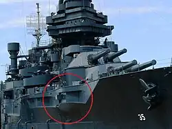 A permanently docked museum ship with a red circle on the photograph to highlight a gun protruding from an opening in the ship's port side.