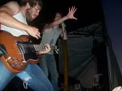 Two men performing onstage, one playing a guitar and the other singing into a microphone