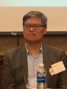 Headshot of Shih, who is in front of a computer projection and behind a water bottle