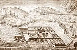 Engraving showing a Carthusian monastery situated at the foot of hills and surrounded by a wall.