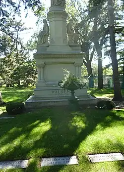 Large stone monument with two women facing opposite directions and another figure cut off at top, in a green cemetery. Of the three visible graves, T. B. Walker is at center and Harriet Hulet Walker is at right
