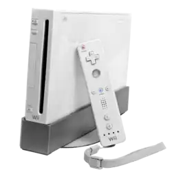 A video game console with mostly white with a glossy finish, featuring a small, vertical form factor. At the front, there is a vertical slot where the discs are inserted. Leaning on the right side is a white, rectangular handheld controller.