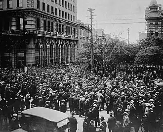 Black and white photo of several hundred people crowding the streets at a downtown intersection