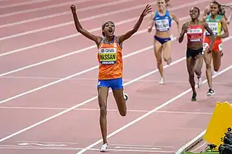 Hassan celebrates crossing the finish line, holding her arms up in front of three other women reaching her.
