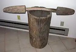 A large wooden mortar with a wooden pestle lying horizontally across the top.