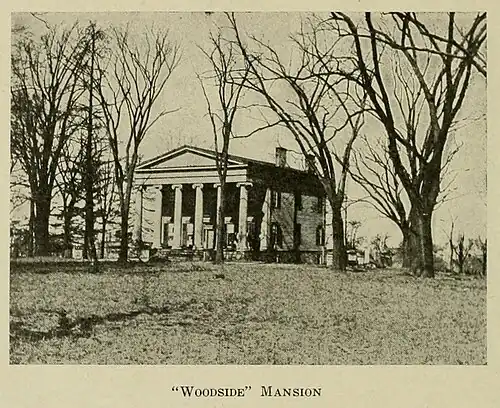 Historical photograph of Woodside Mansion with trees surrounding it. The front of the house has six columns in the Doric style, two stories tall. The ground slopes up gently from the photographer's location to the building.