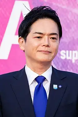 head and shoulders photo of Yamanaka wearing a suit and blue tie, facing camera and looking to right of audience
