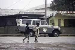 A paved street with a car and two pedestrians.